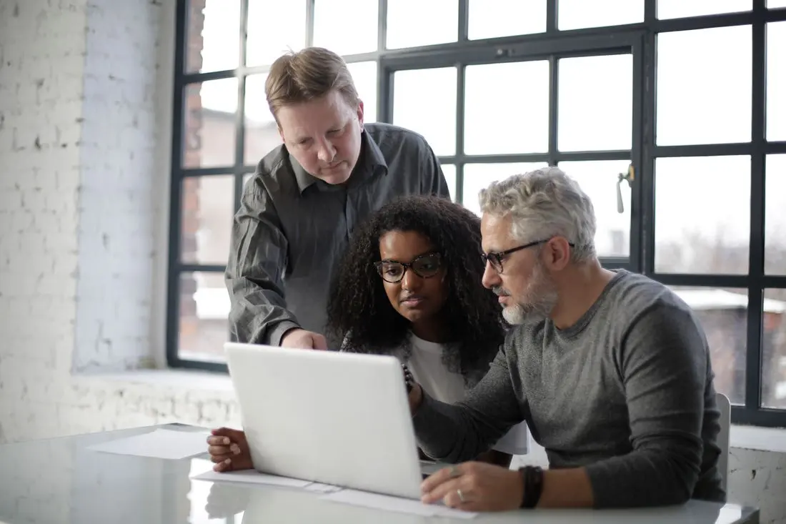 Serious multiethnic coworkers gathering at table for working on laptop and taking about details of project