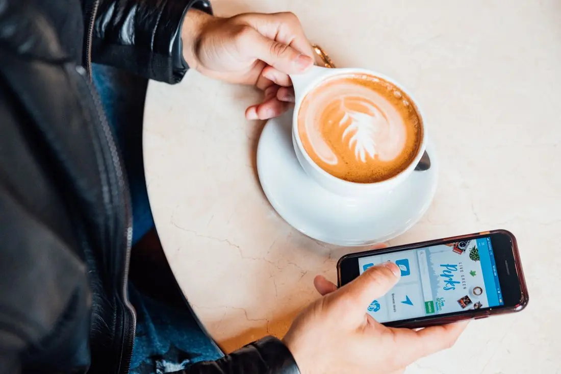 Close-up of person holding latte with beautiful latte art, browsing smartphone