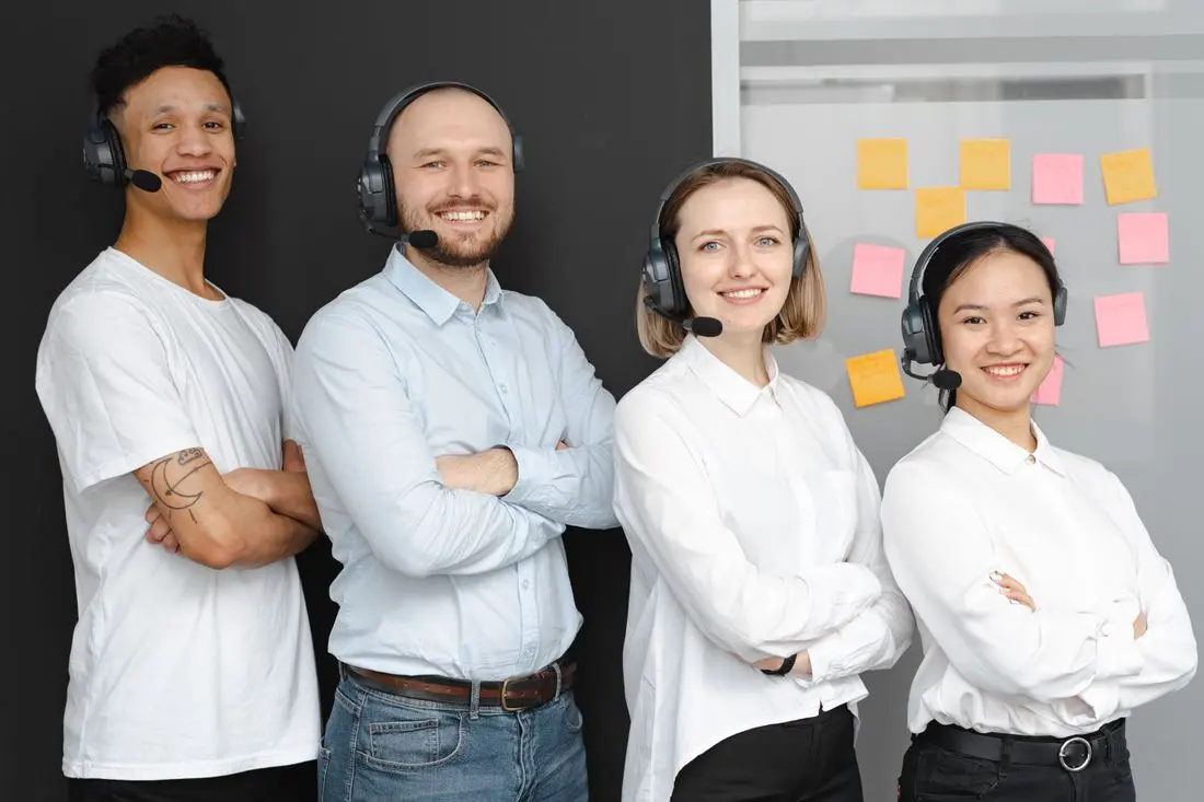 Team of diverse call center professionals smiling and standing confidently with headsets and microphones
