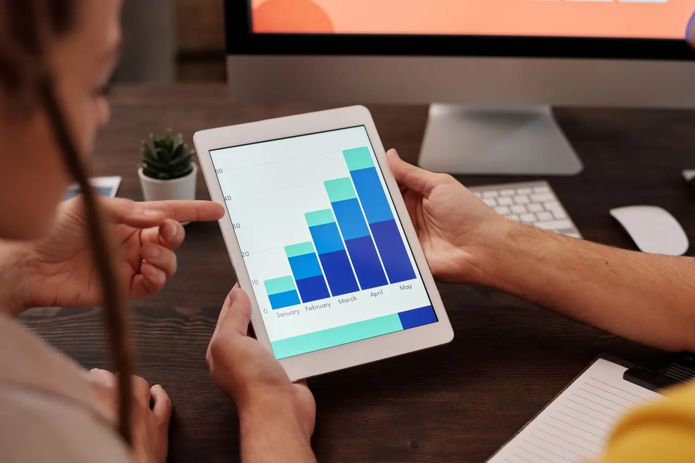Two adults working in an office, examining graphs on a tablet screen for data analysis
