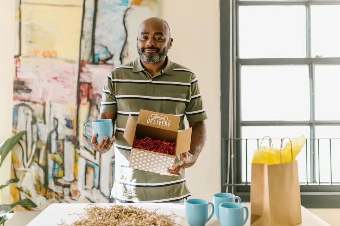 Man packing blue coffee mugs for delivery in a bright, artistic workspace