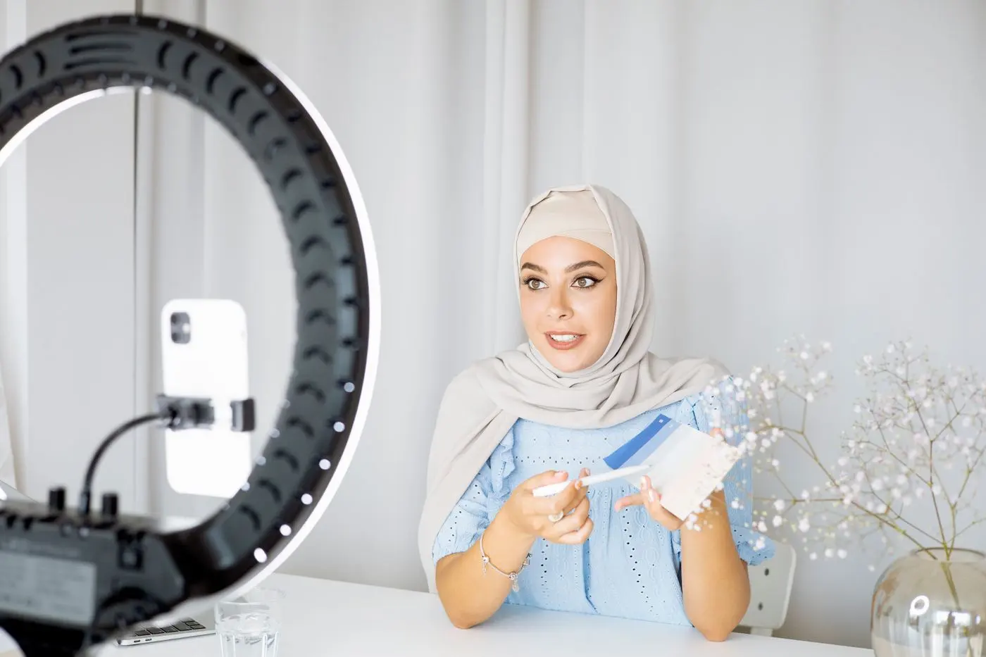 A young Muslim woman using her phone to record a video indoors, with a ring light