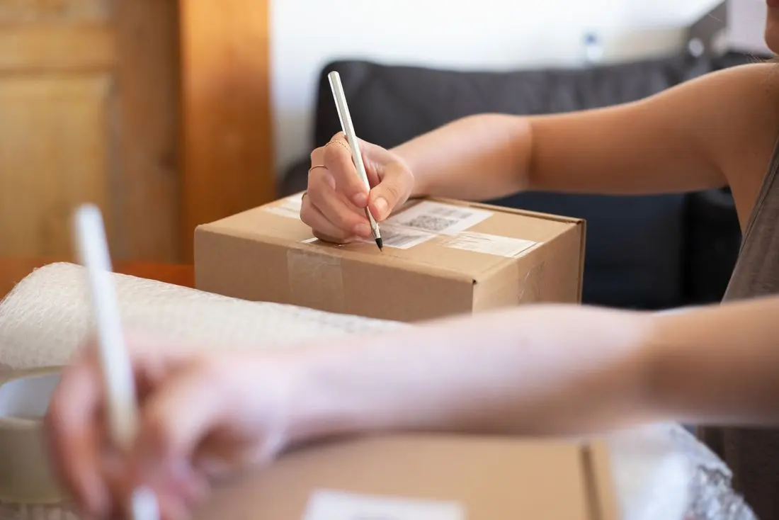 Close-up of hands labeling a cardboard box for online shipping from a home office
