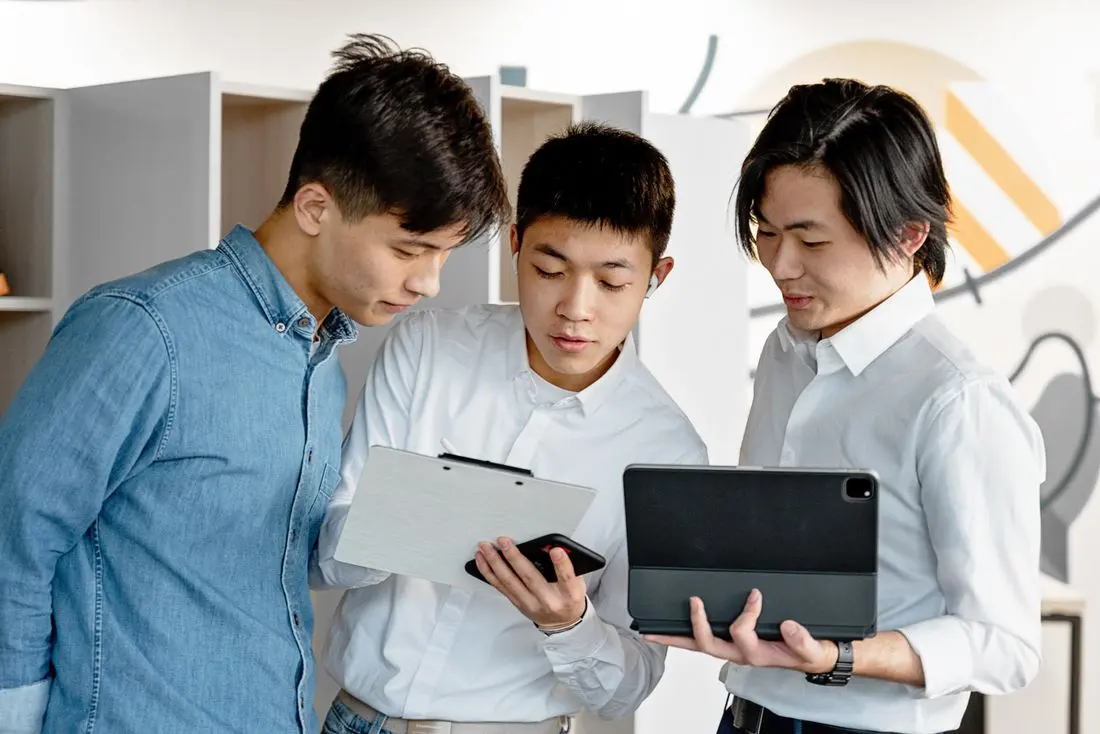 Three young professionals engage in discussion over digital tablets and documents in a modern office setting