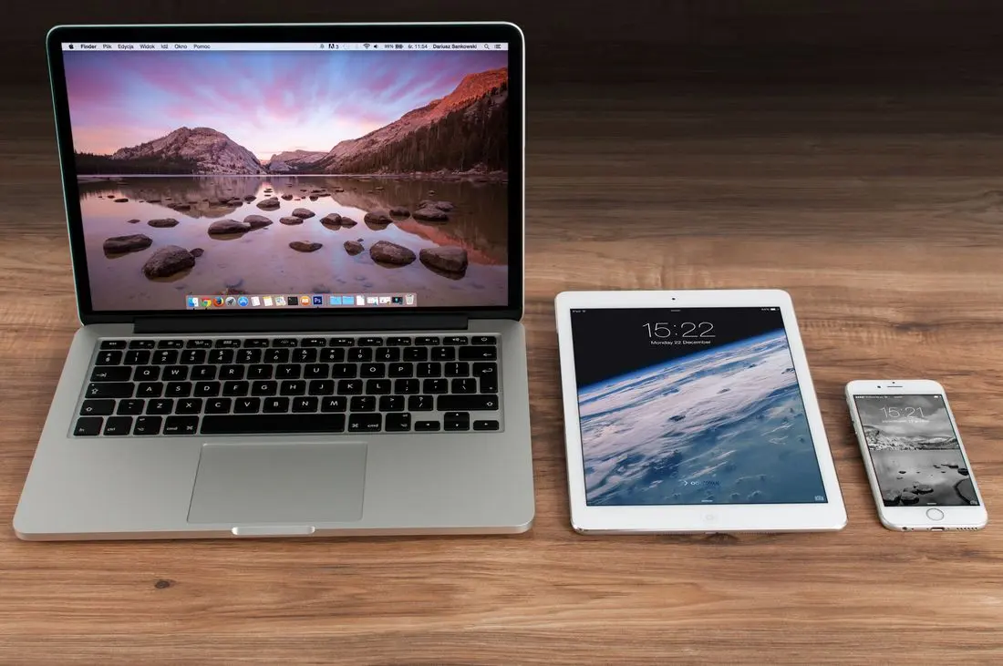 Modern workspace showcasing Apple laptop, tablet, and smartphone on a wooden desk